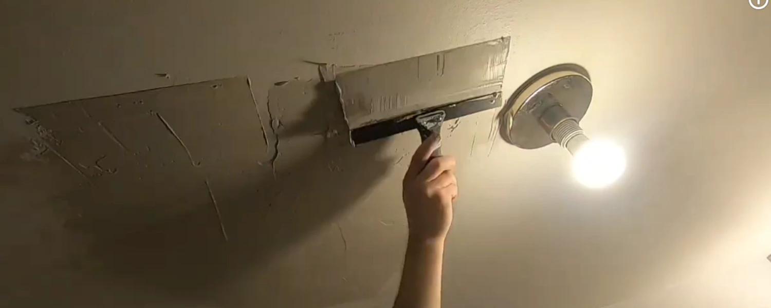 Hand patching a ceiling with a wide drywall knife next to a light fixture