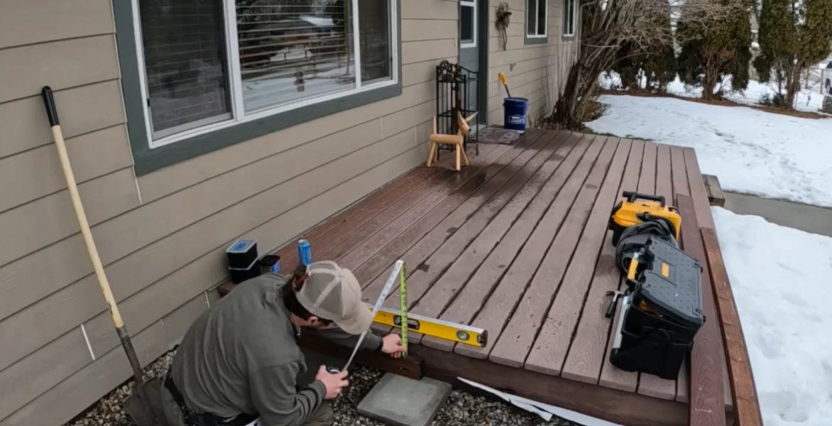 Repair worker measuring a wooden deck with a level and tape measure in winter